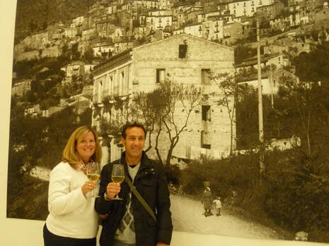 Margaret and Domenico standing in front of an old photo of their B&B, La Rocca Mia House.